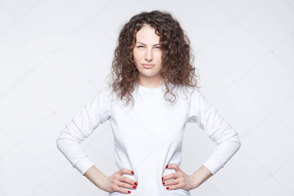Caucasian  brunette female with dark curly hair looks suspiciously into camera, suspects husband in betrayal, going to have scandal, being jealous, isolated over white background. Beauty and youth.