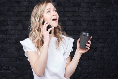 Siyah tuğla stüdyo duvar arka plan, kahve molası sırasında beklenmeyen haber alma biriyle konuşmayı bir elinde kağıt bardak ve diğer, cep telefonu meşgul ABD'li girişimci tutar
