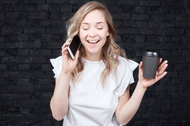 Avukat işkadını professional ile hücre akıllı telefon tek kullanımlık kağıt bardak kahve içme. Genç ve Kapalı gözlerle konuşmayı ayakta tuğla duvar boyunca mutlu beyaz hanımefendi.