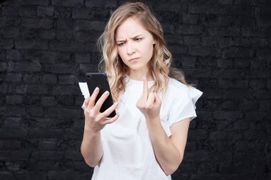Sarışın kadın uzun saçlı, kızgın ifade, telefon, jestleri Studio arayan erkek orta parmak gösterir. Çekici genç bayan lanet işaretleri gösteriyor. Beden dili, teknoloji kavramı.