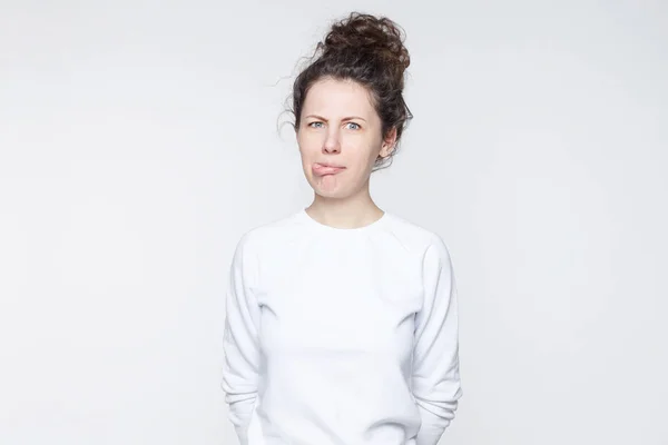 Funny European female with hair bun and charming blue eyes having joy while showing tongue. Cheerful student wearing casual bomber having fun after classes looking and showing tongue at the camera.