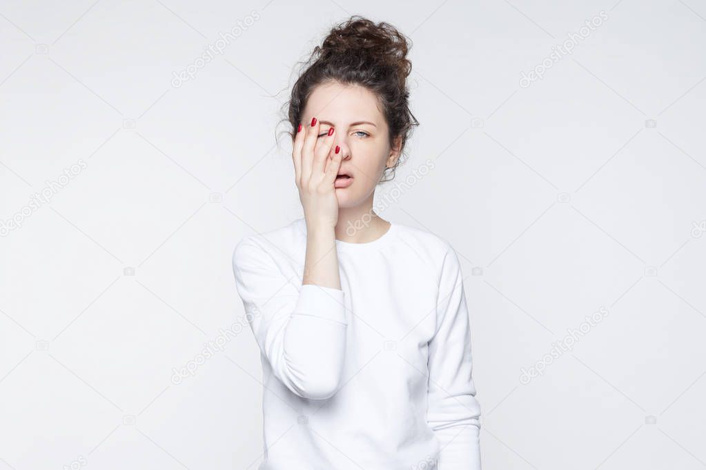 Sad tired sleepy stressful grimacing female with curly hair, keeps hand on cheek, looks desperately, not understands how solve problem, being fatigue after sleepless night. People, tiredness concept