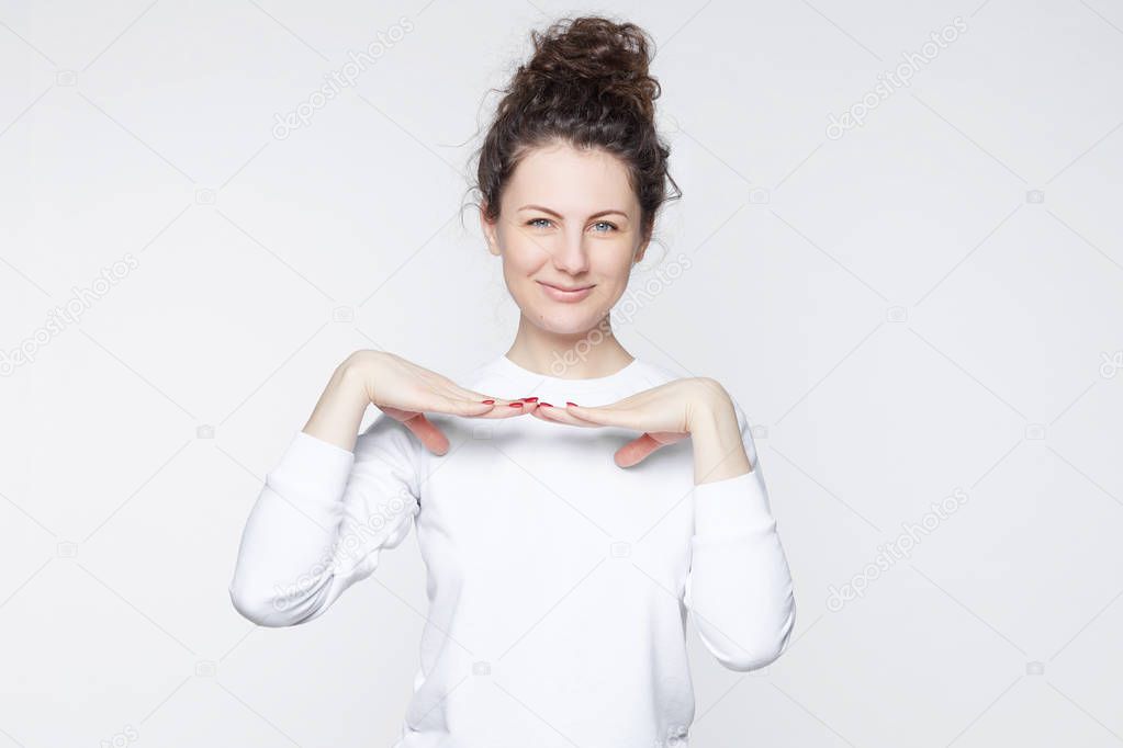Close up portrait of happy curly head young woman looking in excitement holding her both hands under chin imitating indian dance, isolated against white wall. Excited and surprised Caucasian female.