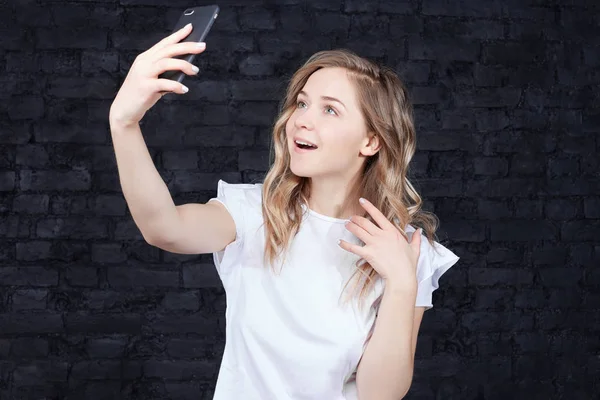 手でスマート フォンのデジタル カメラを押し 黒レンガ壁の背景に Selfie 立って行うのうれしそうな若い女性の肖像画を閉じます ヨーロッパの美しい女性が恋人のために撮影 — ストック写真