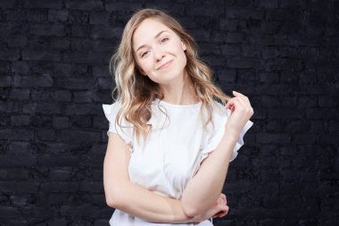 Olumlu insan duyguları. Utangaç göz, kameraya, dalgalı saçları el ile dokunmak şık casual gömlek giymiş gülüyor olan güzel ve çekici kız öğrenci ile zarif saç modeli, portresi.