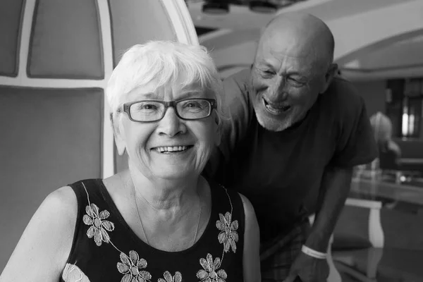 Beautiful lifestyle black and white portrait of European senior couple having fun. Bold man and charming mature woman laughing and playing with each other having good time, enjoying togetherness.