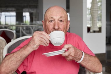 Yakın çekim yakışıklı portresi sakallı kalın eski erkek turistik, kahve molası otel lobisinde, pembe trendy t-shirt giyen sahiptir, bak, yeni hedef keşfetmek gezi için geç kalmaktan korkar mı.