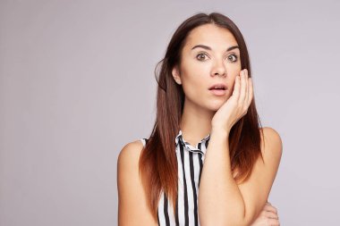 Wondered surprised young woman looks attentively with opened mouth at camera, react on  astonishing news, has long beautiful straight shiny hair, dark brown eyes, wears casual elegant blouse, isolated