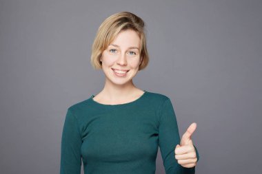 Kısa sarı saçlı neşeli yetişkin kadın samimi duygularını ifade ediyor, mutlu bir şekilde gülümsüyor, fotokopi alanının sahtesini çekiyor, günlük kıyafetler giyiyor, gri stüdyo geçmişine karşı duruyor.. 