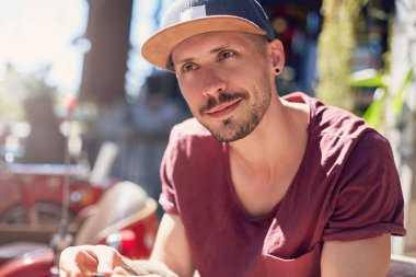 Eski bir dostla açık kafede otururken neşeli bir şekilde gülümseyen neşeli Amerikalı genç adamın gündüz renkli portresini kapat. Seçici odak, film efekti.