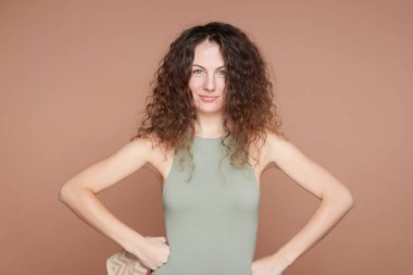 İnsanlar, spor, güç konsepti. Kıvırcık saçlı, mavi gözlü, beyaz dişinin kollarını kalçalarında tutmasına, pazılarını göstermesine, kaslarını göstermesine, ince vücuduna sahip olmasına, bej rengi duvarda mankenler giymesine seviniyorum..