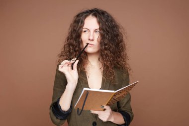 Çekici, kıvırcık saçlı, düşünceli bir yüzü, çekici bir görünüşü var. Elinde kalemle sarmal bir not defteri var. Kompozisyon yazmayı düşünüyor..