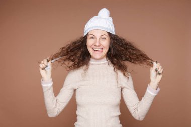 Yaramaz komedyen kadın dil uzatır, yaramazlık yapar, itaatsizlik eder, protesto eder, komik bir görünüşü vardır, şık kışlık kıyafetler giyer, bej renkli stüdyo duvarında izole olur. İnsan yüz ifadeleri.