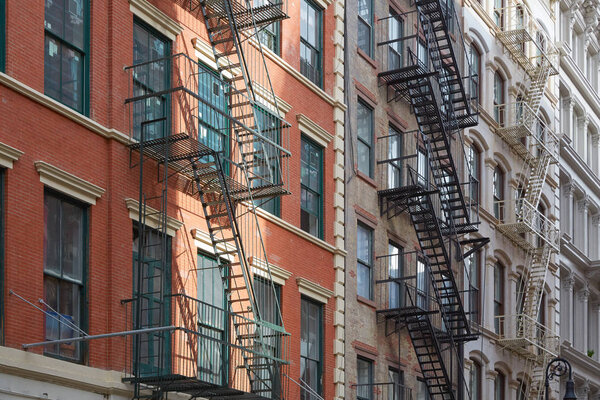 Typical building facades with fire escape stairs, sun beam in Soho, New York