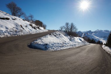 İki taraf, mavi gökyüzü ve güneş kar ile boş dağ yolu eğrisi