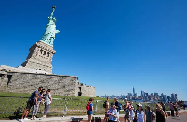 Туристы делают селфи и прогуливаются возле Статуи Свободы в солнечный день, чистое голубое небо — стоковое фото