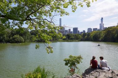 New York'taki Central Park'ta gölet yakınındaki kayaların üzerinde oturan insanlar