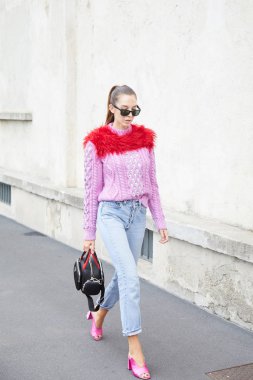 Pembe kazaklı ve kırmızı kürklü kadın Prada defilesinden önce yürüyor, Milan Moda Haftası tarzı. 