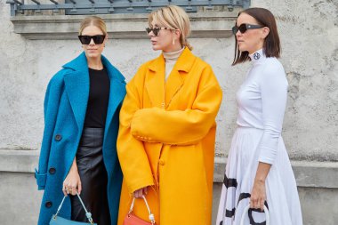 Prada defilesinden önce mavi, turuncu ceketli ve beyaz elbiseli kadınlar, Milan Moda Haftası tarzı. 