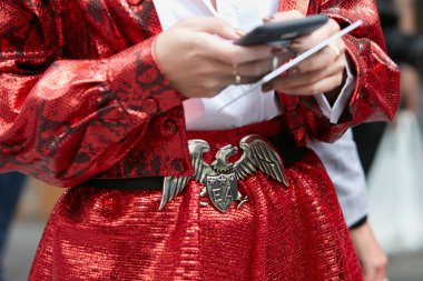 Emporio Armani kemerli, kartal ve kırmızı etekli kadın Emporio Armani moda defilesinden önce akıllı telefona bakıyor, Milan Moda Haftası tarzı. 