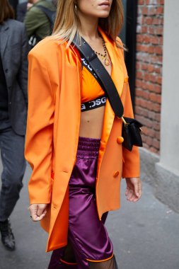 Fendi defilesinden önce turuncu ceketli ve mor pantolonlu kadın, Milan Moda Haftası tarzı. 