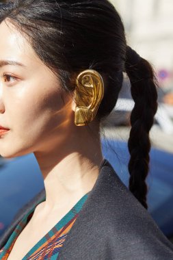 Salvatore Ferragamo moda defilesinden önce kulak şeklinde altın küpeli kadın, Milan Moda Haftası tarzı. 