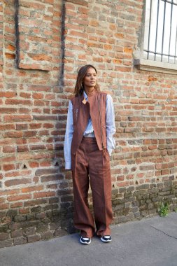 Salvatore Ferragamo defilesinden önce kahverengi pantolonlu ve ceketli kadın, Milan Moda Haftası tarzı. 