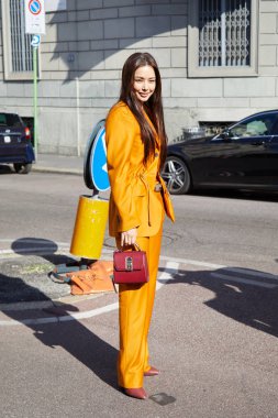 Salvatore Ferragamo moda defilesinden önce turuncu ceketli, pantolonlu ve Ferragamo deri çantalı kadın, Milan Moda Haftası tarzı. 