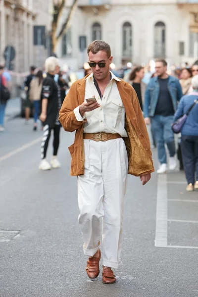 Homem andando com casaco de camurça marrom e calças brancas olhando para o smartphone antes Giorgio Armani desfile de moda, estilo de rua Milan Fashion Week — Fotografia de Stock