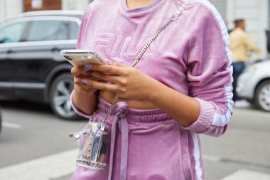 Mor kadife takımlı ve şeffaf çantalı kadın Fila defilesinden önce akıllı telefona bakıyor, Milan Moda Haftası tarzı.