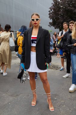 Fila defilesinden önce beyaz pileli etekli ve siyah ceketli kadın, Milan Moda Haftası tarzı. 