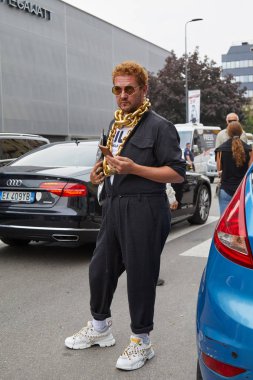 Fila defilesinden önce siyah tulumlu ve altın kolyeli bir adam, Milan Moda Haftası tarzı. 