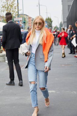 Gucci moda defilesinden önce turuncu kazaklı, gri ceketli ve kot pantolonlu kadın, Milan Moda Haftası tarzı. 