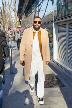 Emporio Armani moda defilesinden önce bej ceketli ve beyaz pantolonlu bir adam, Milan Moda Haftası tarzı. 
