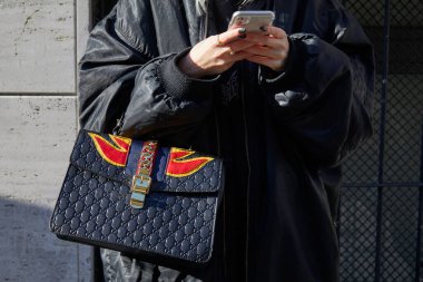 Gucci siyah deri çantalı, kırmızı ve sarı alevli kadın Etro defilesinden önce akıllı telefona bakıyor, Milan Moda Haftası tarzı. 