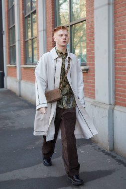 Fendi defilesinden önce beyaz önlüklü ve kahverengi çantalı bir adam, Milan Moda Haftası tarzı.