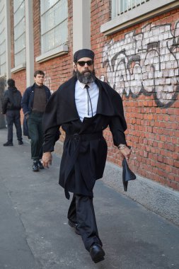 Siyah Prada şapkalı ve pelerinli adam Fendi defilesinden önce yürüyor, Milan Moda Haftası tarzı.