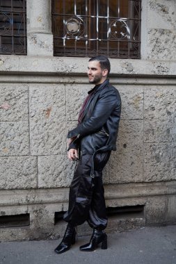 Reshake defilesinden önce siyah deri ceketli ve yüksek topuklu ayakkabılı bir adam, Milan Moda Haftası tarzı.