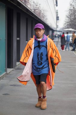 Marco de Vincenzo moda defilesinden önce turuncu yağmurluk ve mor şapkalı bir adam, Milan Moda Haftası tarzı.