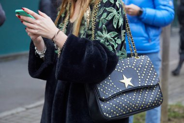 Marco de Vincenzo moda defilesinden önce siyah deri çantalı ve yıldızlı bir kadın akıllı telefona bakıyordu. Milan Moda Haftası tarzı.