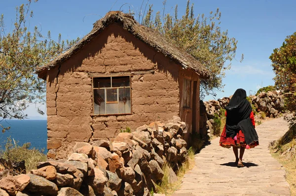 Local woman passing by a typical house in Taquile Island, Titicaca Lake, Peru