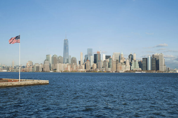 New York City, New York, USA - November 21, 2015: View towards Freedom tower and financial district from Upper Bay Hudson River with the American flag on the left-hand side situated on Ellis Island.