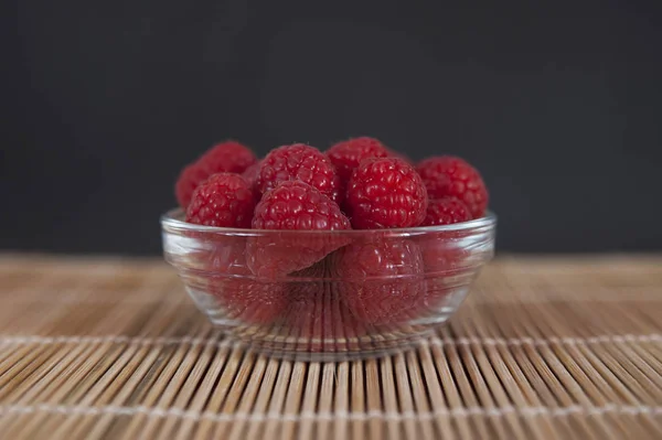 Verse frambozen in een kom geplaatst op een bamboe mat tegen een donkere achtergrond — Stockfoto