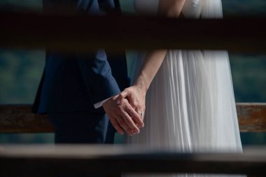 Kırpılmış, paparazzi tarzı, beyaz ipeksi bir elbise giymiş beyaz bir gelin ve damadın el ele tutuşup, güzel bir çiftin düğün öncesi yakınlık kurduğu özel bir fotoğraf.