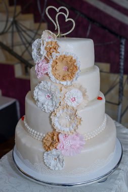 Çiçekler, yenilebilir dantel ve inciler ayrıntıları ve kalp şeklindeki topper dört katmanlı düğün pastası ile pastel renkli