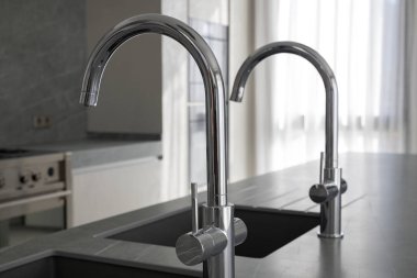 Modern kare mutfak lavaboları ve koyu gri granit mutfak adasına yerleştirilmiş krom musluklar, dayanıklı malzemeler ve çağdaş aletler kullanarak evler için lüks ve minimalist tasarım