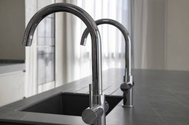 Modern kare mutfak lavaboları ve koyu gri granit mutfak adasına yerleştirilmiş krom musluklar, dayanıklı malzemeler ve çağdaş aletler kullanarak evler için lüks ve minimalist tasarım