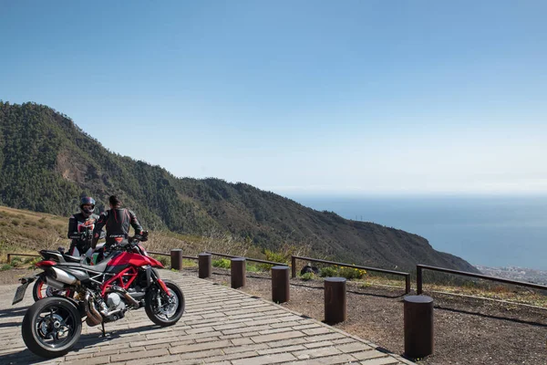 TF-523 Yolu ya da Carretera Los Loros, Tenerife, Kanarya Adaları, İspanya - 12 Mart 2020: İki genç motosikletçi dinlenmek ve panoramik manzaranın tadını çıkarmak için Mirador de Chivisaya 'da durdu