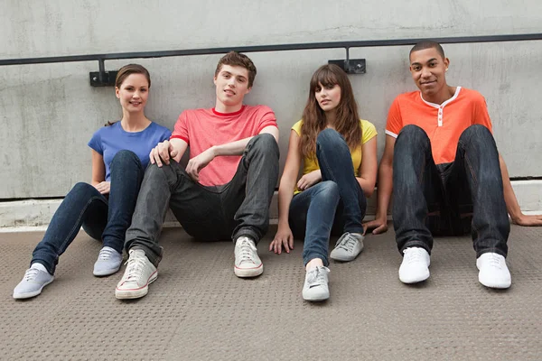 Jóvenes sentados en fila contra la pared — Foto de Stock