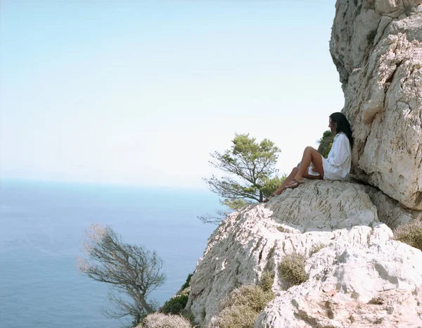 Женщина, сидящая на больших камнях у моря — стоковое фото